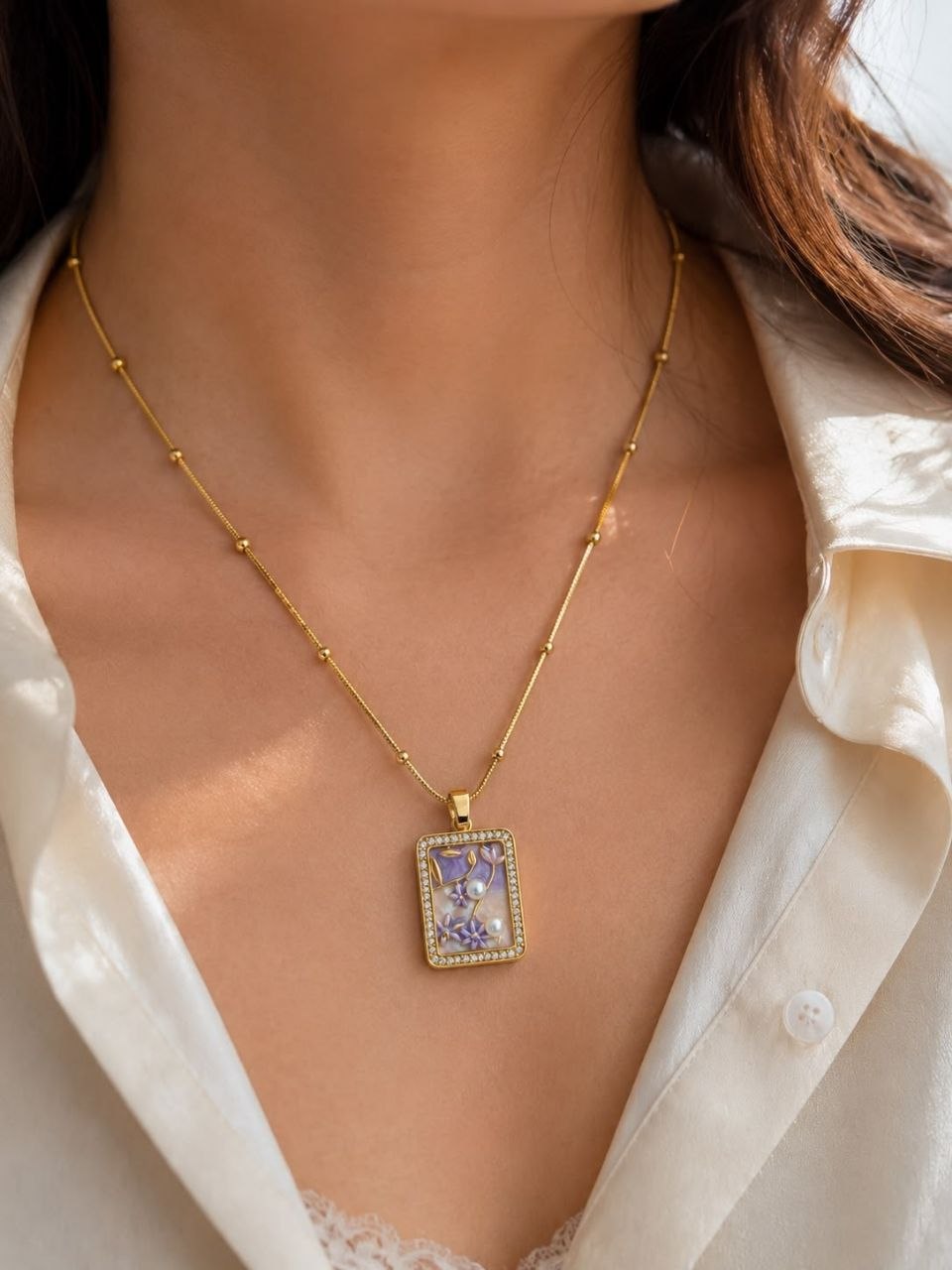 Gold beaded chain necklace with rectangular pendant featuring purple floral design, white pearls and crystal border on white satin fabric 2