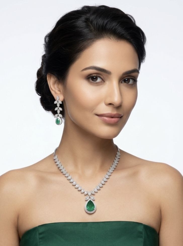 Luxury silver necklace with large green emerald teardrop pendant and matching dangling earrings featuring leaf motif cubic zirconia stones on white fabric 2