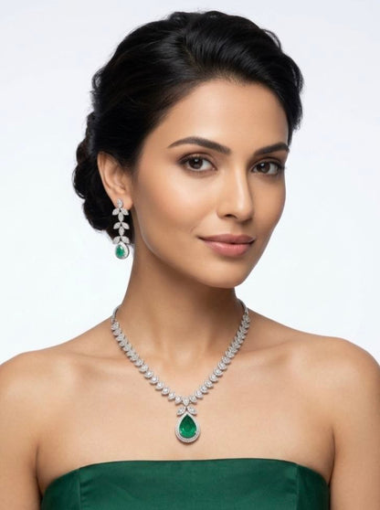Luxury silver necklace with large green emerald teardrop pendant and matching dangling earrings featuring leaf motif cubic zirconia stones on white fabric 2