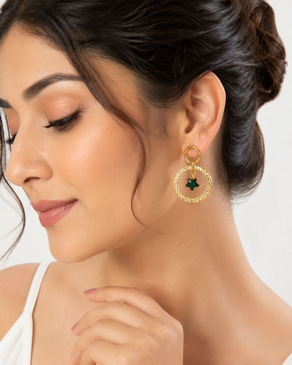 Pair of gold hammered circular hoop earrings with dangling green star crystal pendants on white background 2