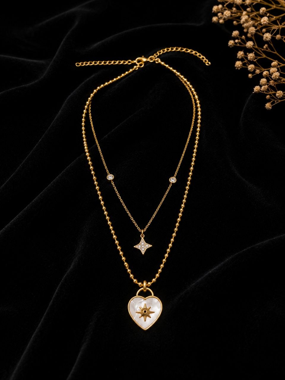 Premium gold layered necklace with white mother of pearl heart pendant featuring starburst design and small crystal star pendant on beige background 3