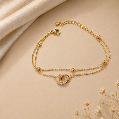 Premium gold bracelet with two interlocking circles one encrusted with sparkling crystals on delicate chain with gold bead accents displayed on white fabric 3