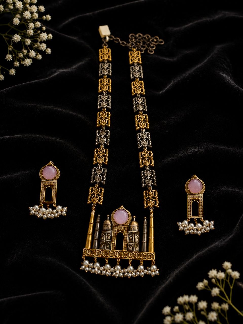 Antique gold and black Taj Mahal motif necklace with pink stone pendant and pearl drops alongside matching earrings on beige fabric with white flowers 3
