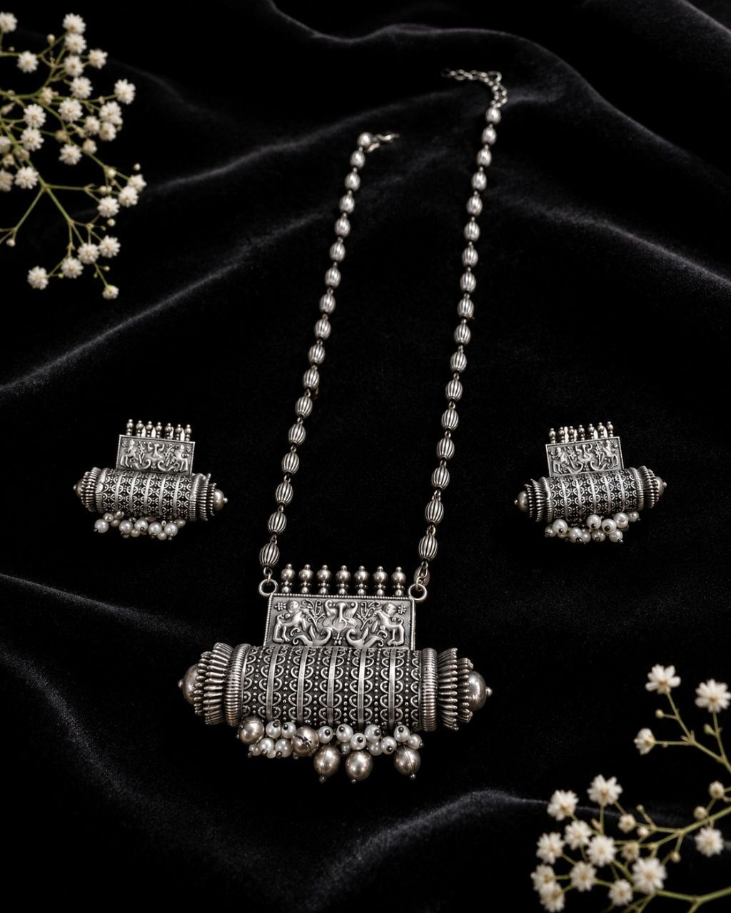 Oxidized silver necklace with detailed elephant pendant and dangling pearl beads paired with matching earrings on beige background 3