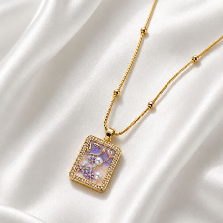 Gold beaded chain necklace with rectangular pendant featuring purple floral design, white pearls and crystal border on white satin fabric 1
