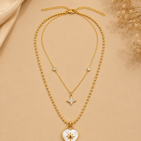 Premium gold layered necklace with white mother of pearl heart pendant featuring starburst design and small crystal star pendant on beige background 1