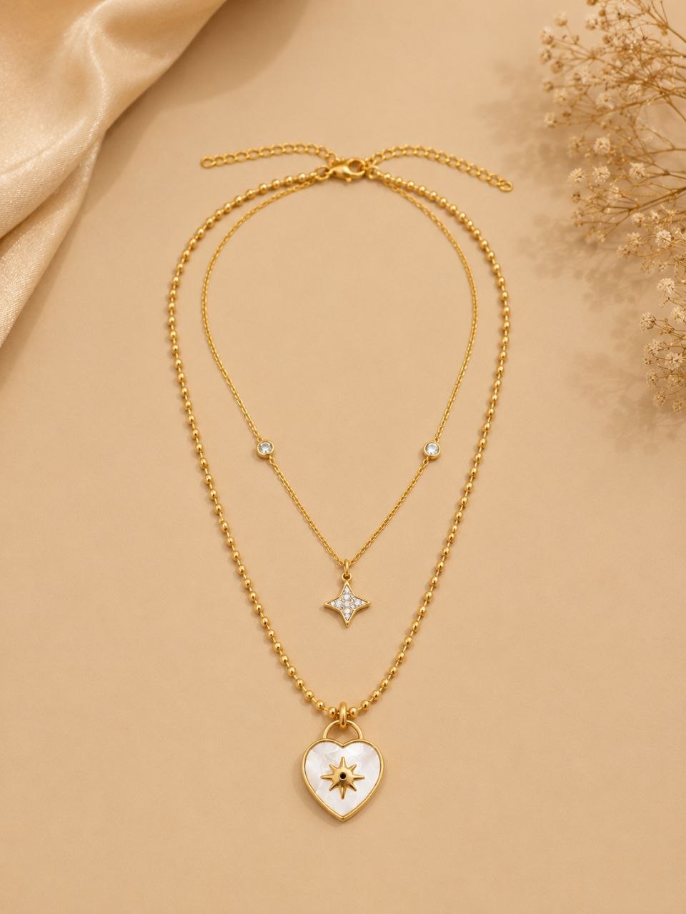Premium gold layered necklace with white mother of pearl heart pendant featuring starburst design and small crystal star pendant on beige background 1