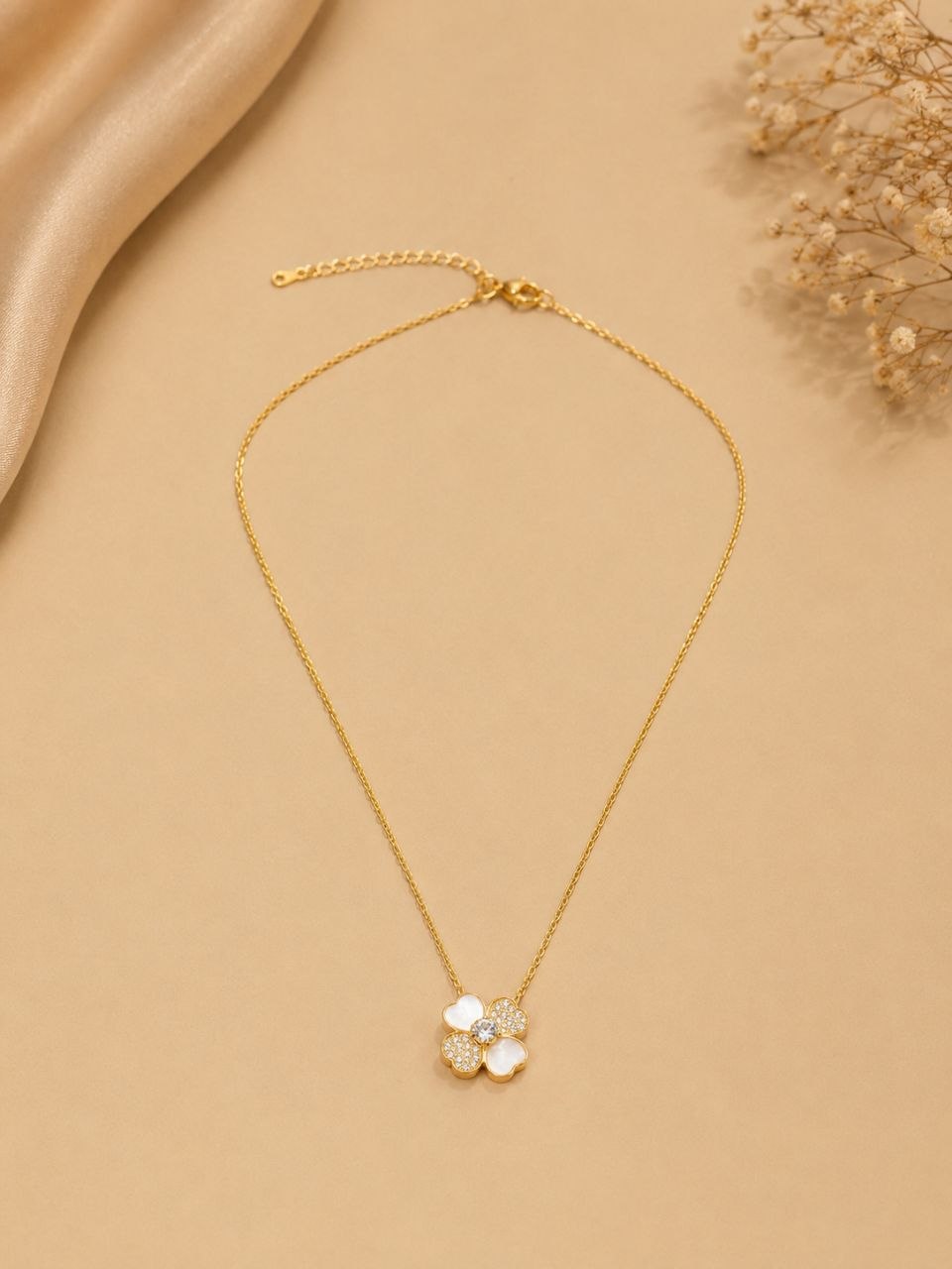 Delicate gold chain necklace with white four-petal floral pendant featuring sparkling crystal stones on beige background 1
