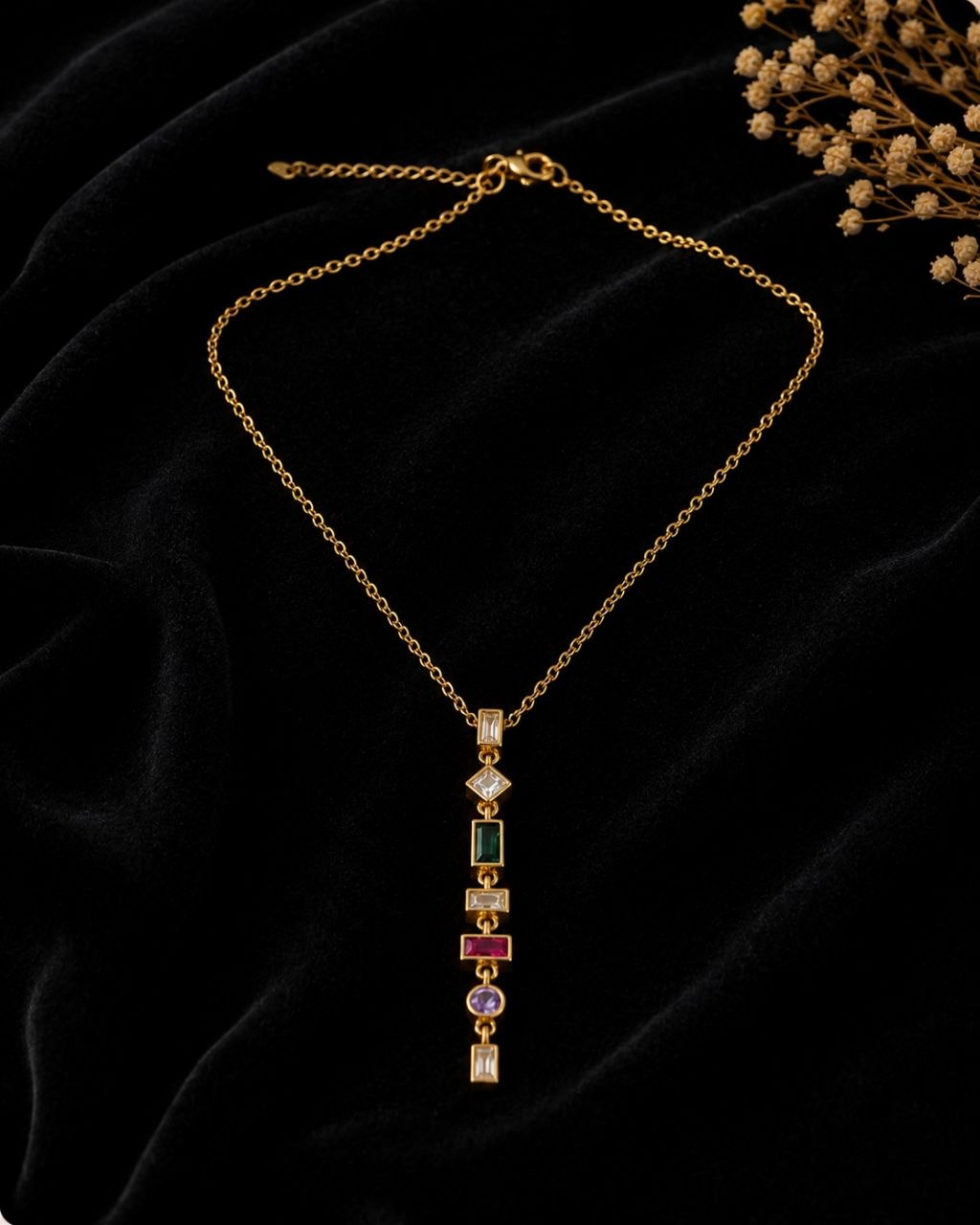 Gold necklace with vertical multicolour gemstone pendant featuring green, pink, purple and clear stones on beige background 3