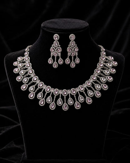 Elegant silver-plated necklace with pink teardrop cubic zirconia stones and matching chandelier earrings displayed on a beige jewelry bust against a soft beige background 3