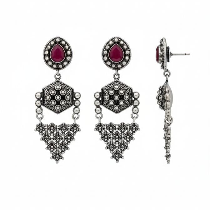 Pair of traditional Indian oxidized silver drop earrings with red teardrop gemstones, hexagonal middle motifs and intricate filigree triangular danglers on white background 1