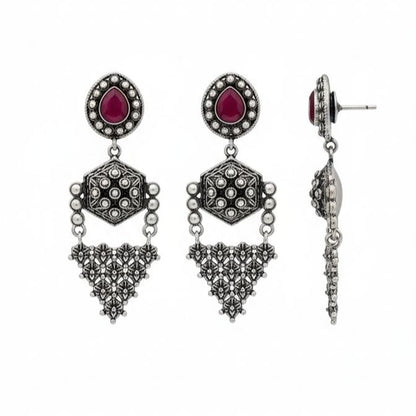 Pair of traditional Indian oxidized silver drop earrings with red teardrop gemstones, hexagonal middle motifs and intricate filigree triangular danglers on white background 1
