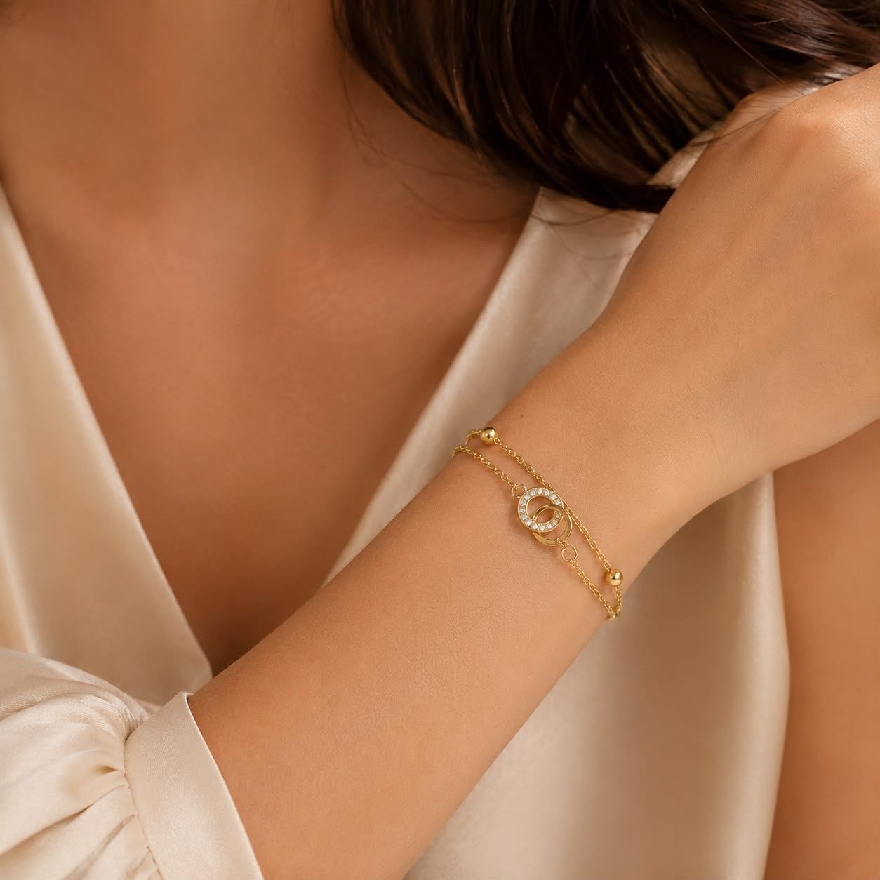 Premium gold bracelet with two interlocking circles one encrusted with sparkling crystals on delicate chain with gold bead accents displayed on white fabric 2