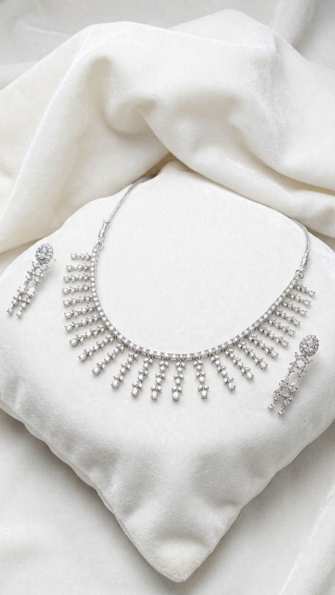 Premium silver fringe necklace with cascading crystal tassels and matching drop earrings displayed on white velvet fabric 1