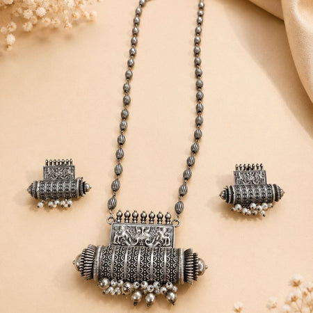 Oxidized silver necklace with detailed elephant pendant and dangling pearl beads paired with matching earrings on beige background 1