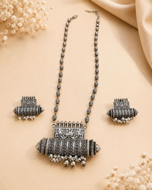 Oxidized silver necklace with detailed elephant pendant and dangling pearl beads paired with matching earrings on beige background 1