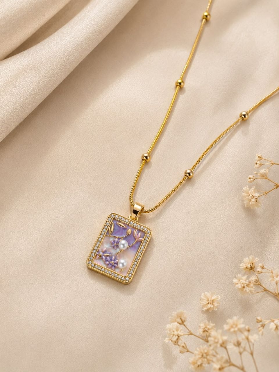 Gold beaded chain necklace with rectangular pendant featuring purple floral design, white pearls and crystal border on white satin fabric 3