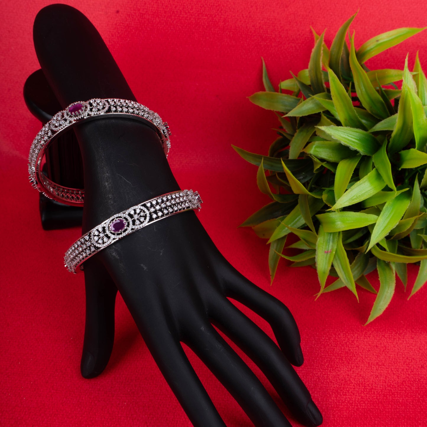 Silver bangle with oval ruby centerpiece and intricate stone detailing on red background - Revaaj