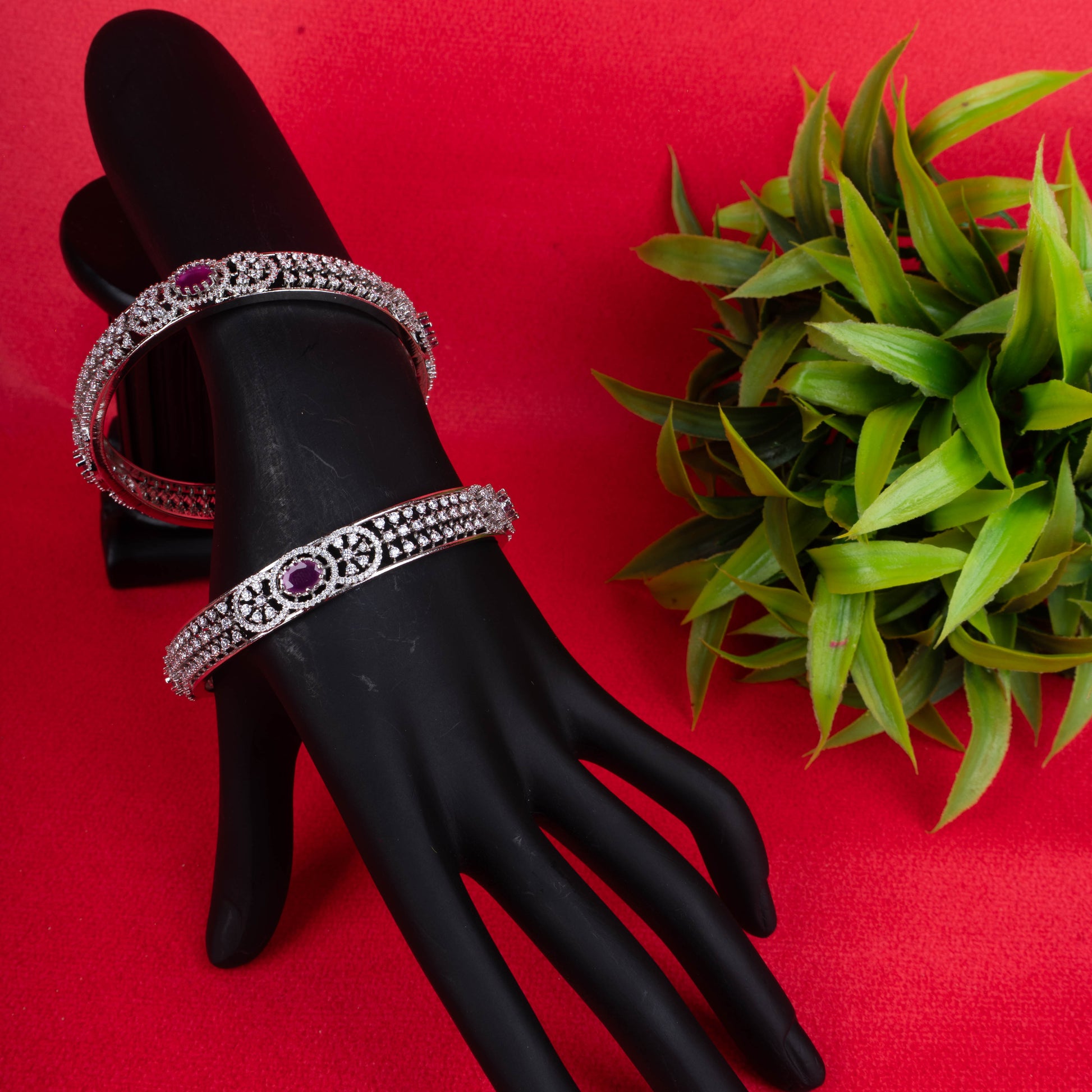 Silver bangle with oval ruby centerpiece and intricate stone detailing on red background - Revaaj