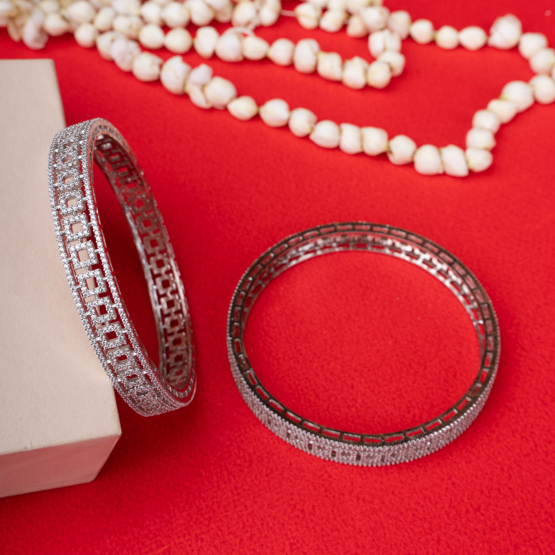 Silver geometric cut bangles with crystal detailing on red background - Revaaj