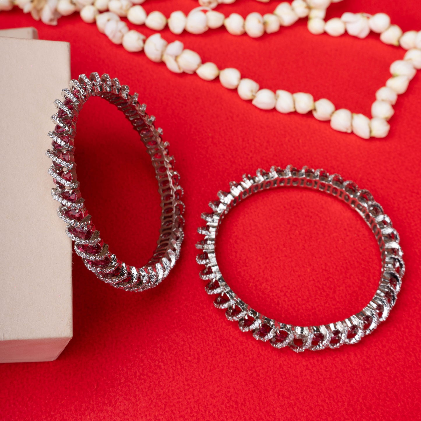 Silver looped crystal bangles with twisted stone design on red background - Revaaj