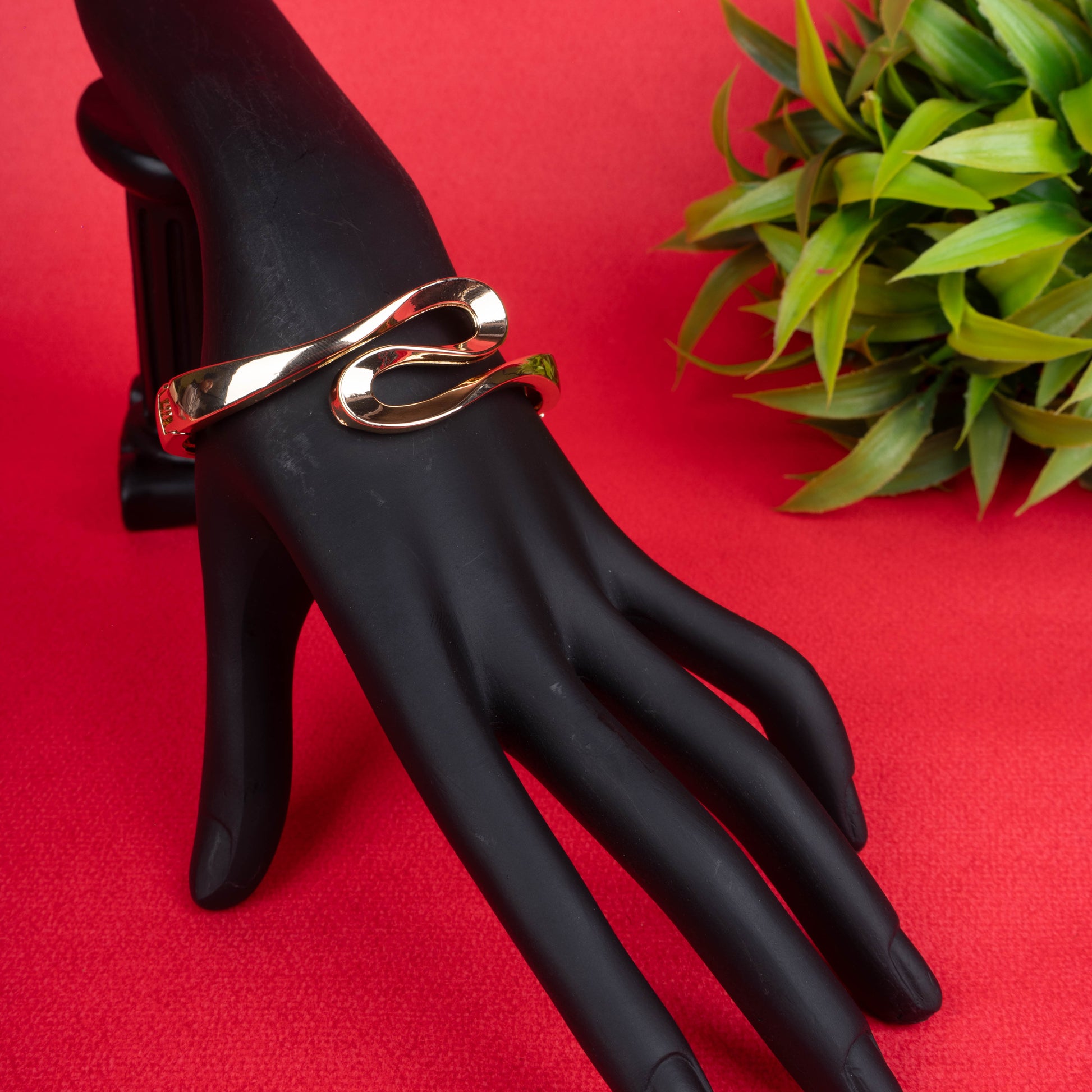 Gold-tone open cuff bracelet with a sculptural, looping design on a black mannequin hand - Revaaj