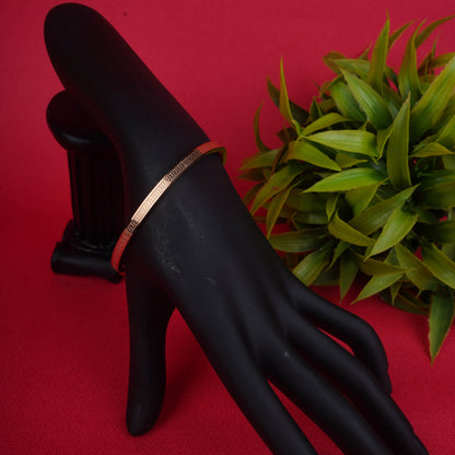 Gold-tone bangle bracelet with a continuous Greek key pattern etched into the surface, shown on a black mannequin hand - Revaaj