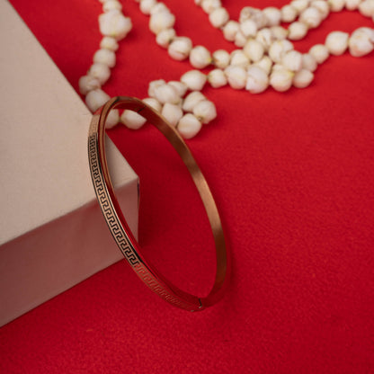 Gold-tone bangle bracelet with a continuous Greek key pattern etched into the surface, shown on a black mannequin hand ground image - Revaaj