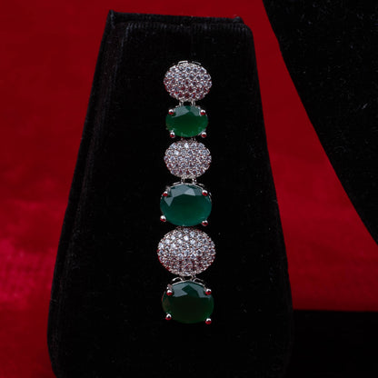 Earring with alternating green stones and clear crystal-studded round links on black velvet with red background