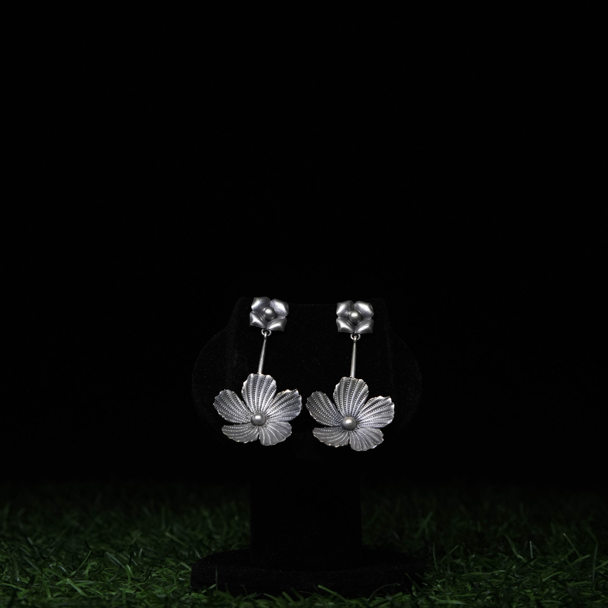Oxidized silver floral dangler earrings with intricate petal design displayed on black stand