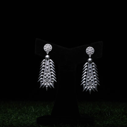 Tribal oxidized silver statement earrings with elongated design and spiked edges displayed on black stand