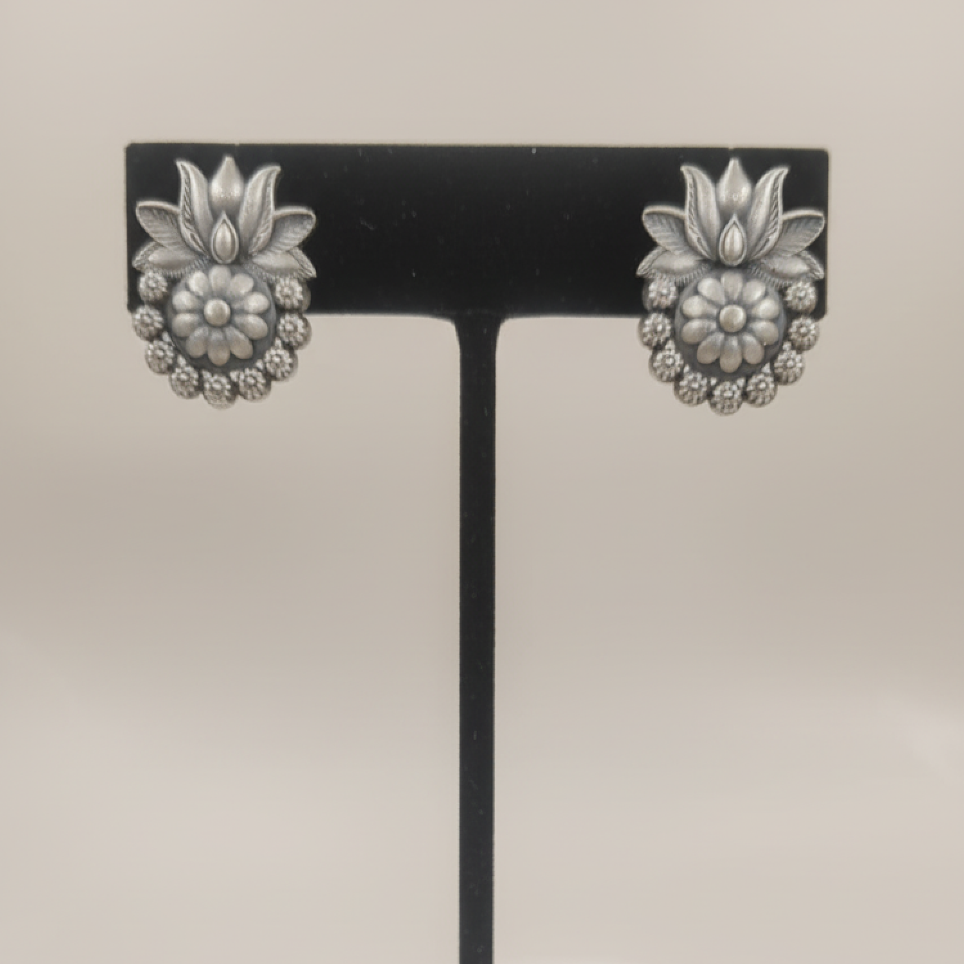 Oxidized silver floral stud earrings with intricate design displayed on a black stand