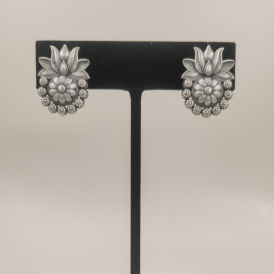 Oxidized silver floral stud earrings with intricate design displayed on a black stand