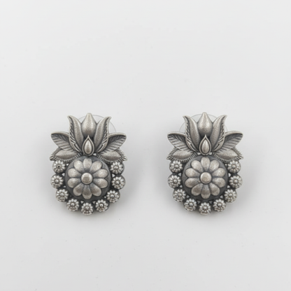 Oxidized silver floral stud earrings with intricate design displayed on a black stand ground