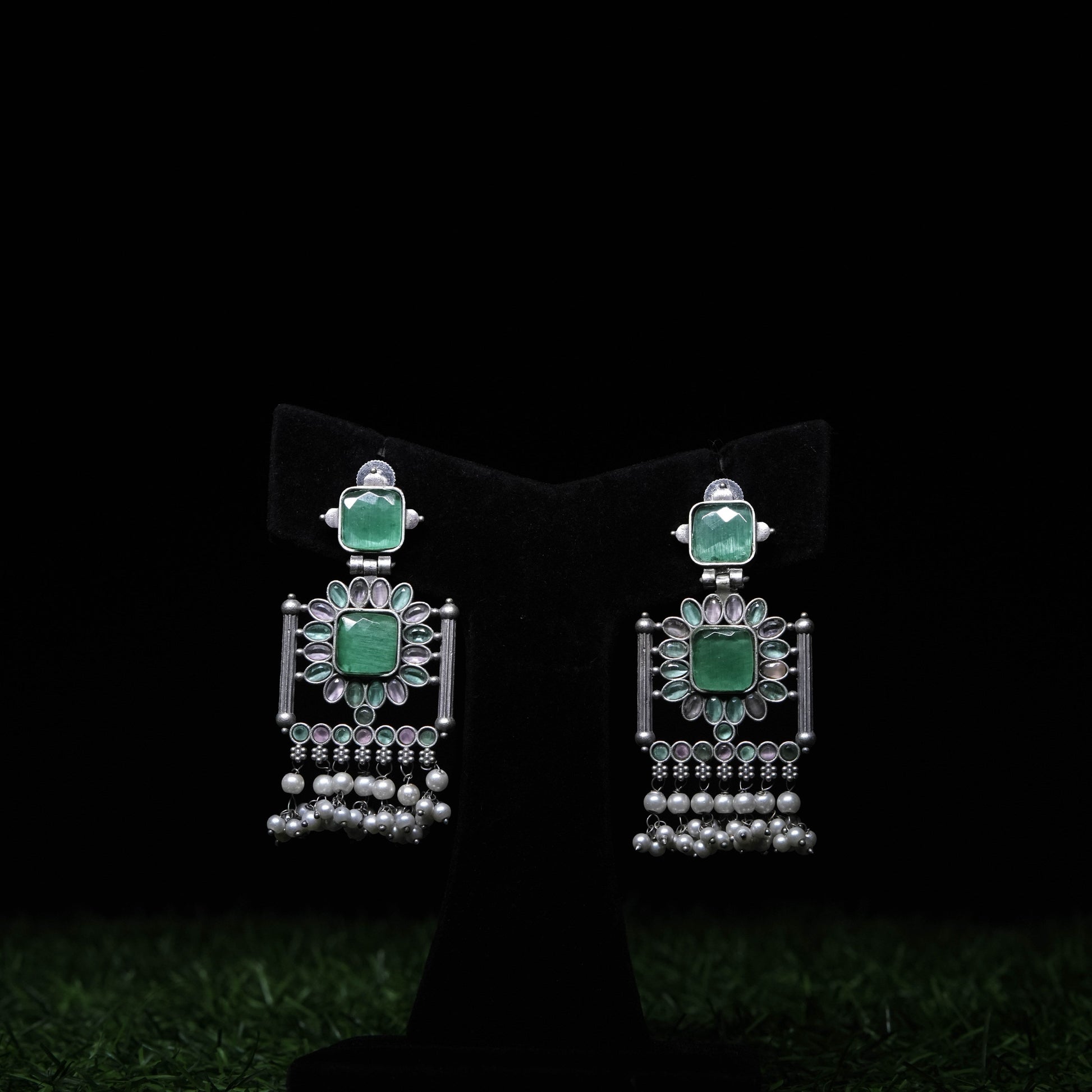 Oxidized silver chandbali earrings with green stones and pearl drops displayed on black stand