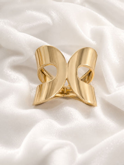 Shiny gold bow-shaped metallic hair claw clip displayed on white satin fabric 1