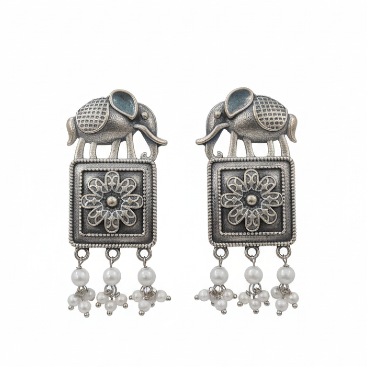 Oxidized silver earrings with elephant motifs, floral square design, and pearl drop detailing displayed on a black stand ground