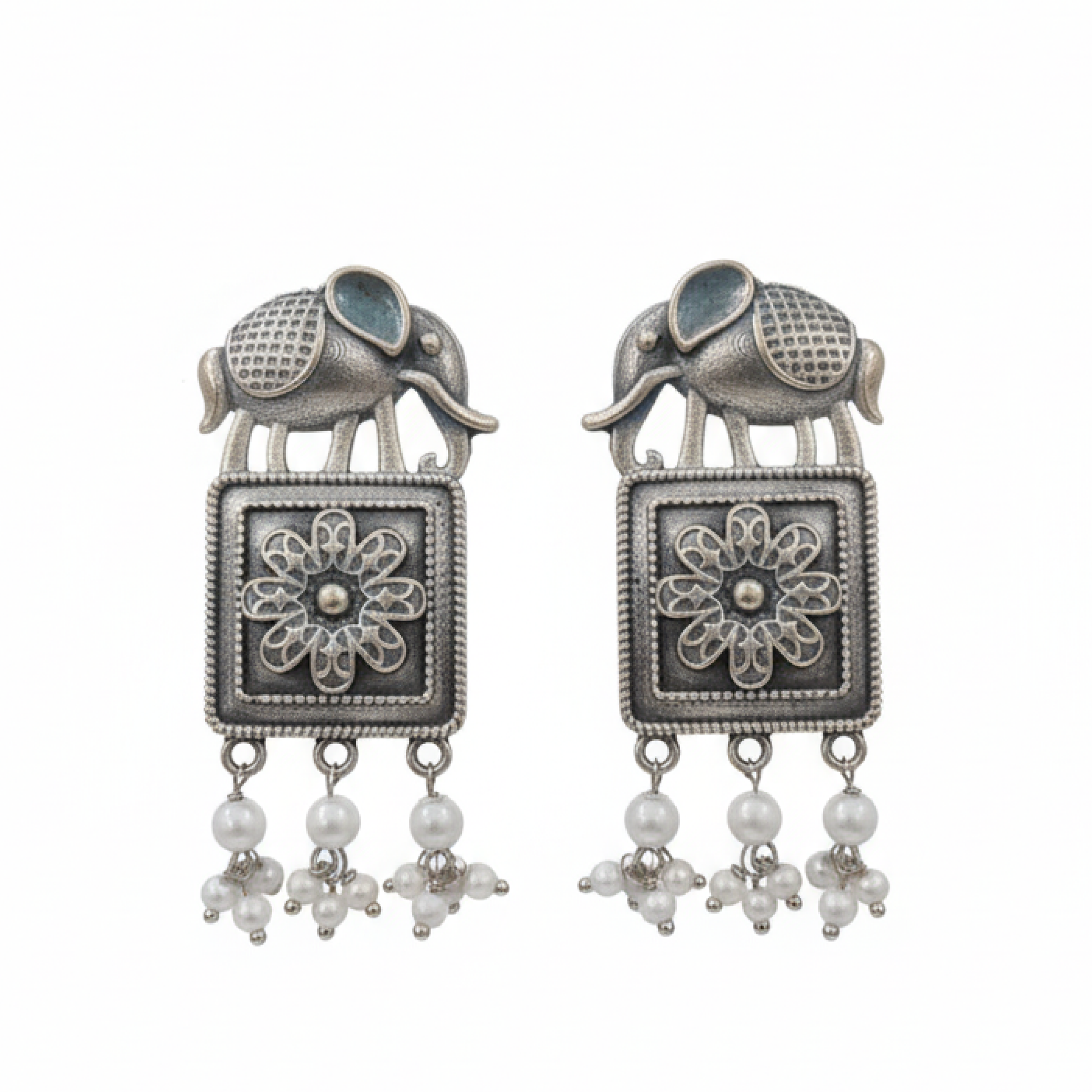 Oxidized silver earrings with elephant motifs, floral square design, and pearl drop detailing displayed on a black stand ground