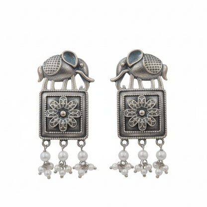 Oxidized silver earrings with elephant motifs, floral square design, and pearl drop detailing displayed on a black stand ground