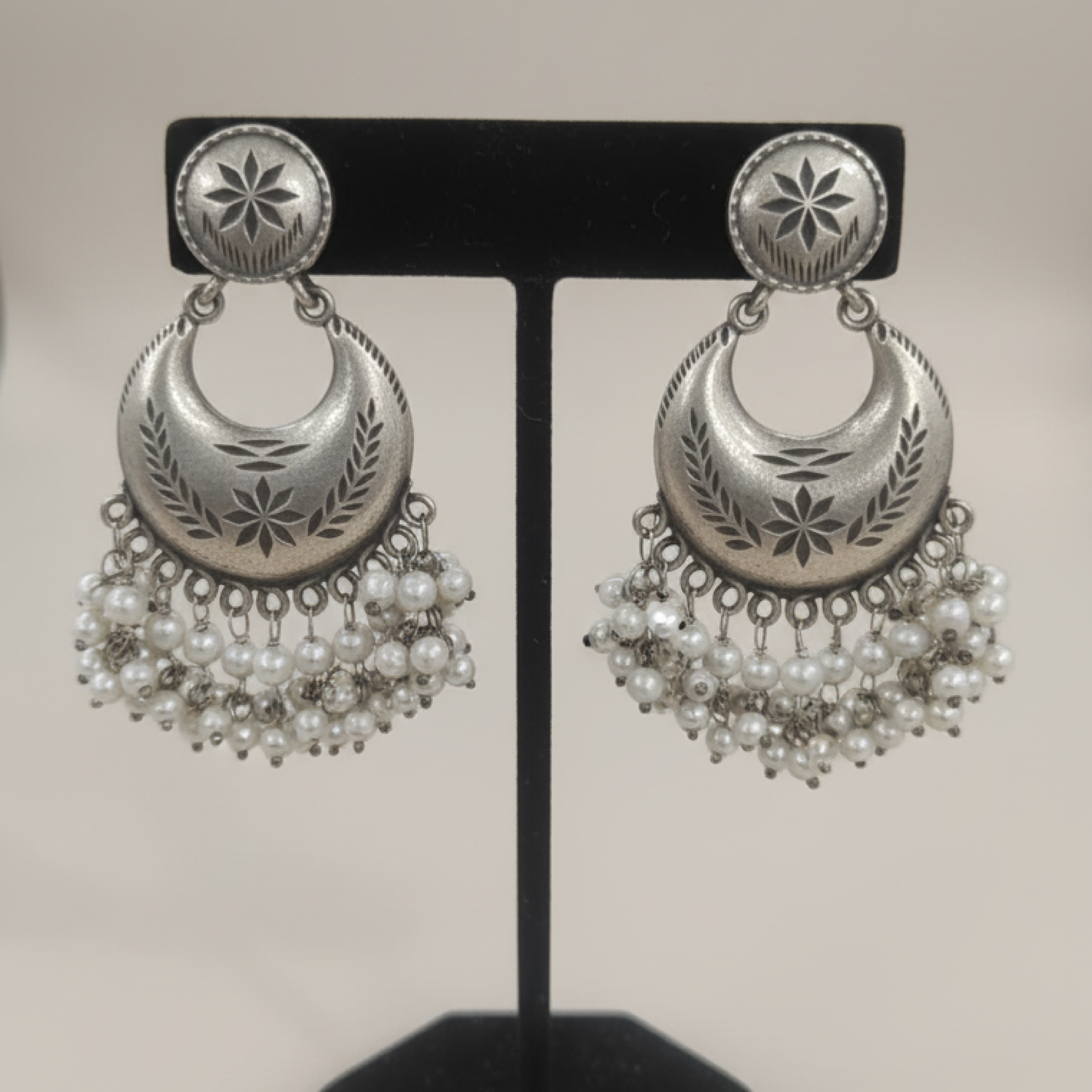 Oxidized silver crescent earrings with engraved detailing and pearl hangings displayed on a black stand