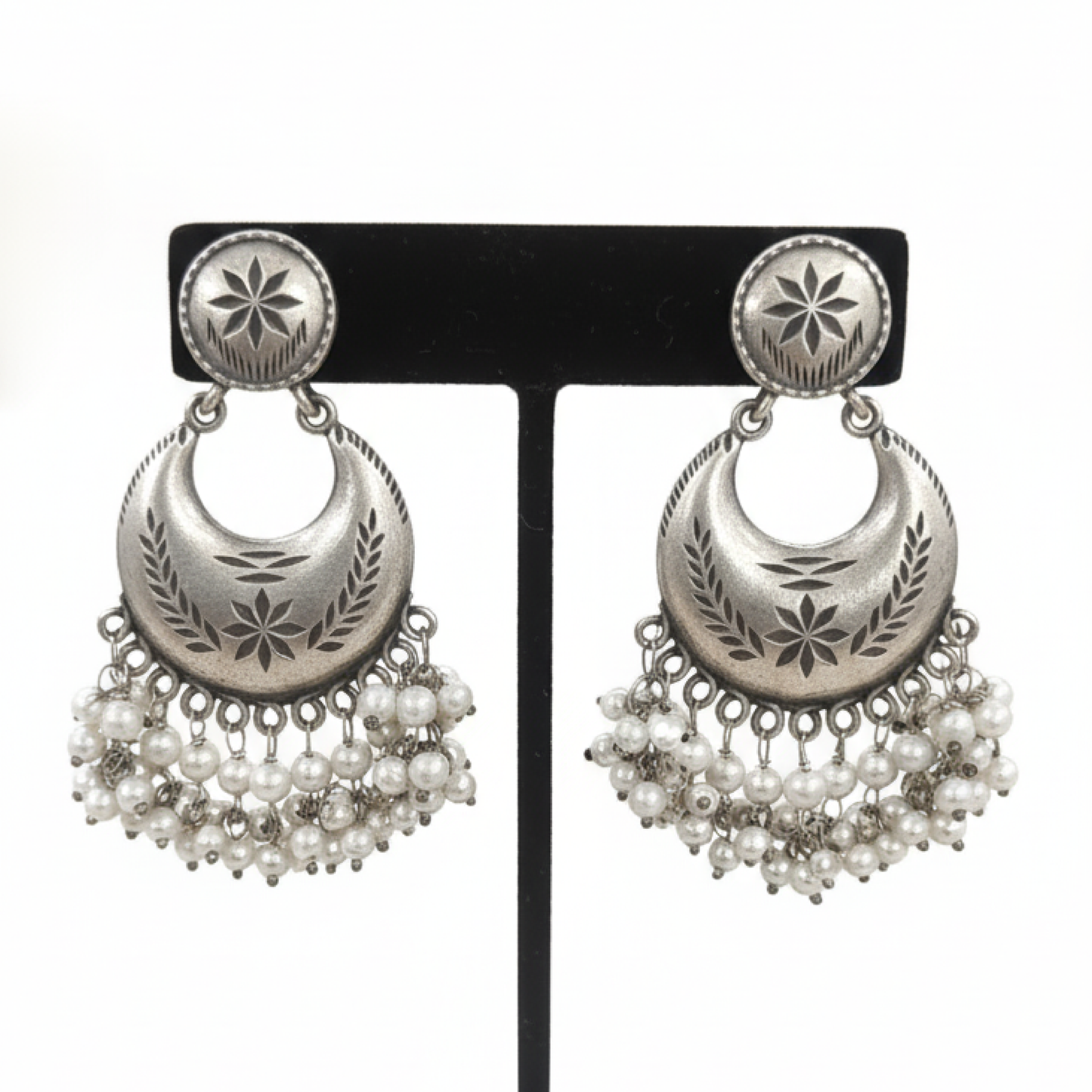 Oxidized silver crescent earrings with engraved detailing and pearl hangings displayed on a black stand ground