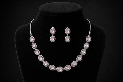 Silver-toned necklace with multiple oval pink gemstones in pave settings paired with matching drop earrings displayed on a beige jewelry bust 2