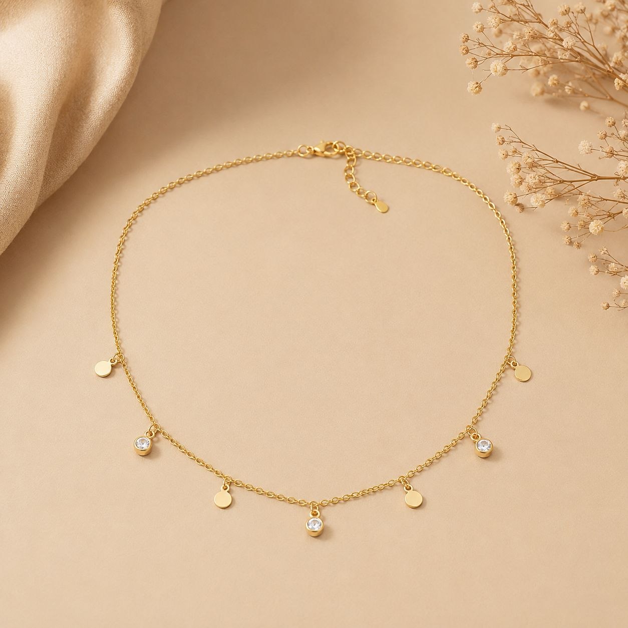 Delicate gold necklace with multiple circular charms and three clear crystal pendants displayed on beige fabric background 1
