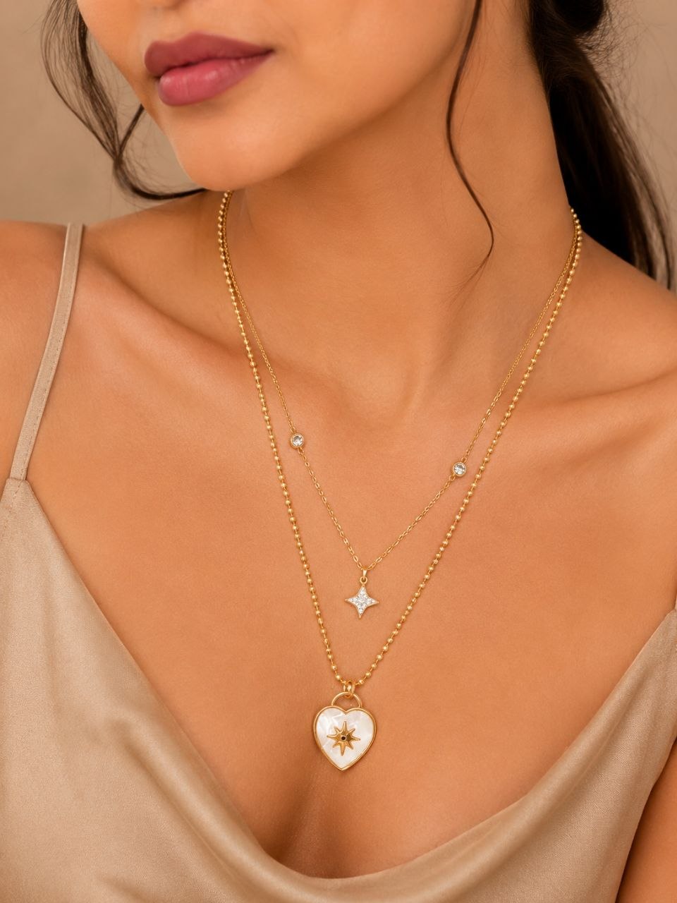 Premium gold layered necklace with white mother of pearl heart pendant featuring starburst design and small crystal star pendant on beige background 2