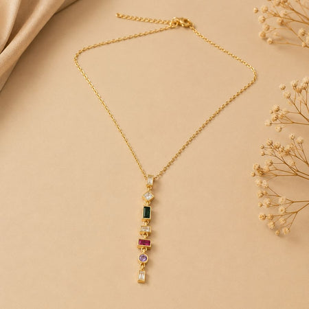 Gold necklace with vertical multicolour gemstone pendant featuring green, pink, purple and clear stones on beige background 1