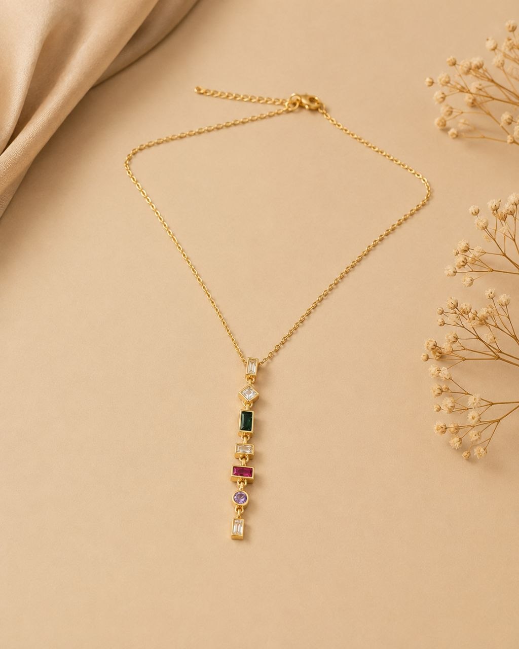 Gold necklace with vertical multicolour gemstone pendant featuring green, pink, purple and clear stones on beige background 1