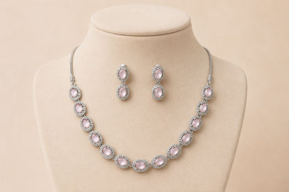 Silver-toned necklace with multiple oval pink gemstones in pave settings paired with matching drop earrings displayed on a beige jewelry bust 1