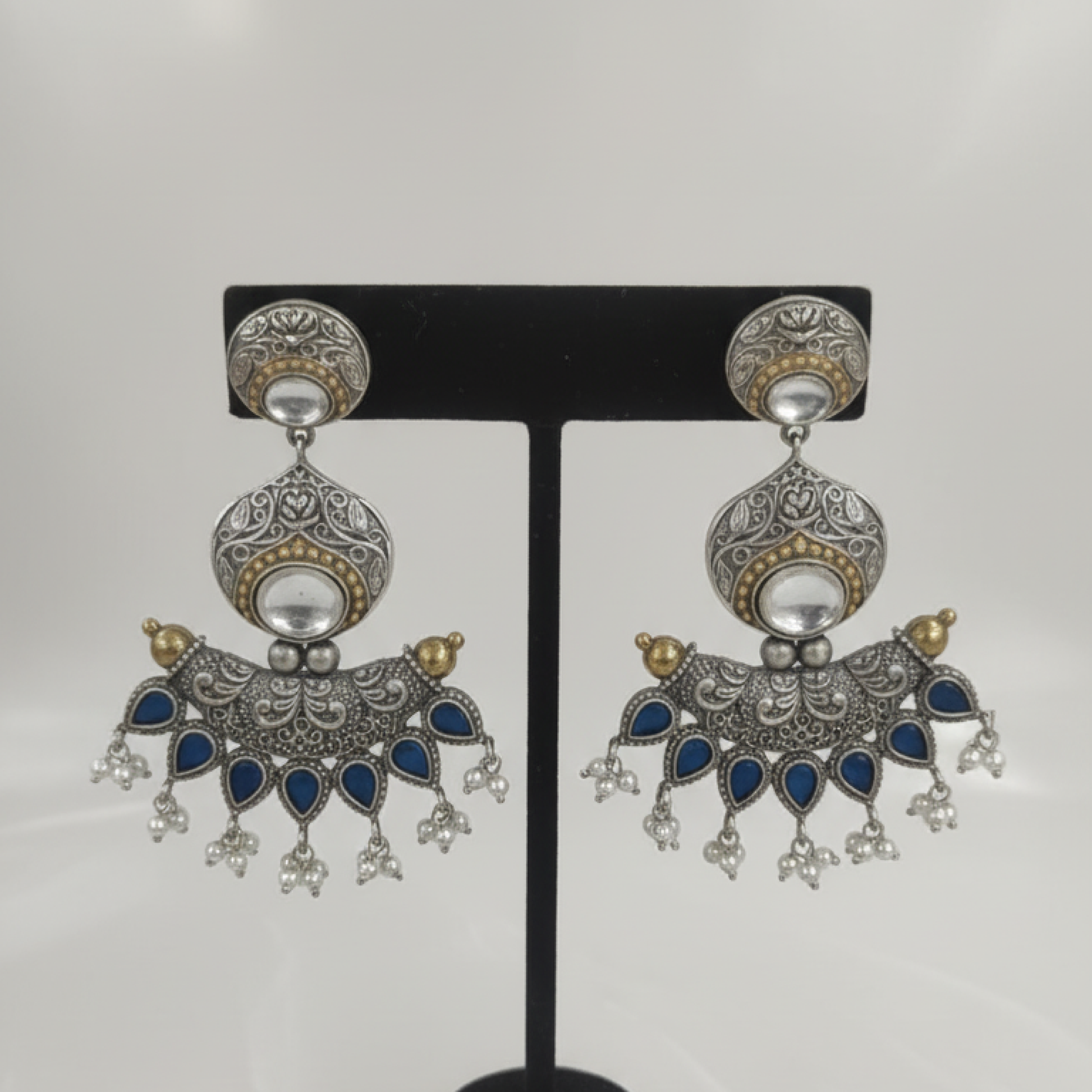 Oxidized silver earrings with blue teardrop stones, intricate filigree work, and pearl hangings on a black display stand