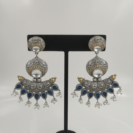 Oxidized silver earrings with blue teardrop stones, intricate filigree work, and pearl hangings on a black display stand