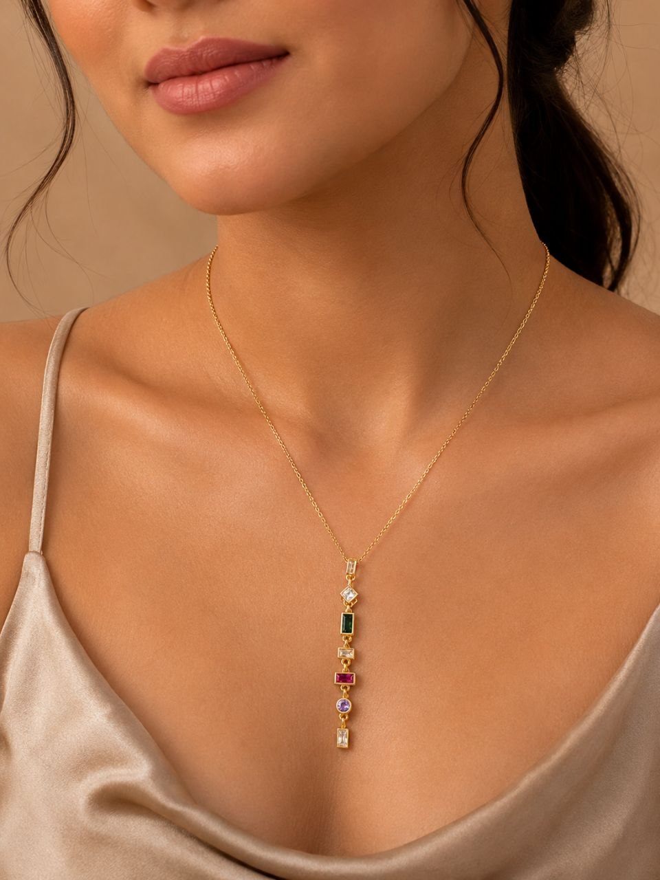 Gold necklace with vertical multicolour gemstone pendant featuring green, pink, purple and clear stones on beige background 2